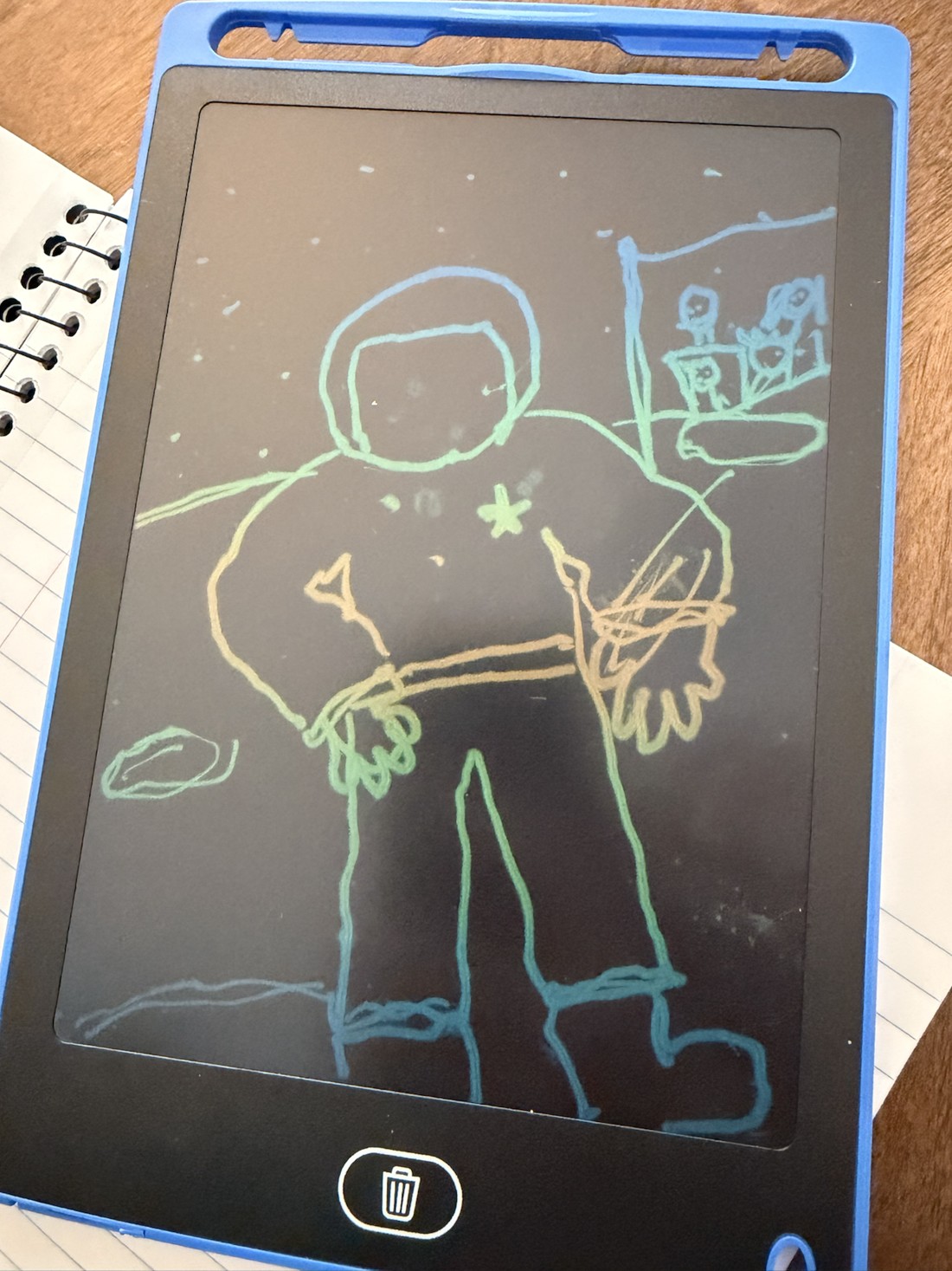 Henry's original drawing on a blue writing tablet: an astronaut with a round helmet, a chest star, large boots, and a family flag.
